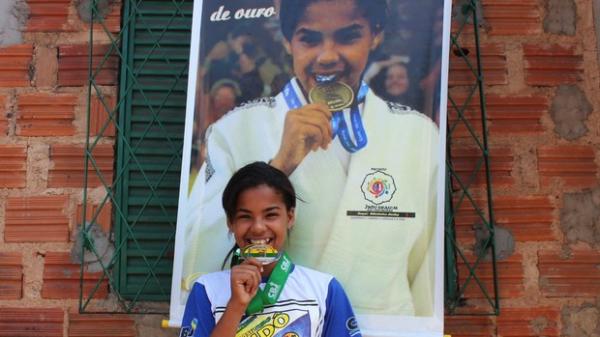 A fama de 'morde medalha' rendeu at&eacute; um presente inusitado dos colegas de treino: um banner com a foto mordendo a medalha de ouro conquistada nos Jogos Escolares.(Imagem:N&aacute;yra Mac&ecirc;do/GLOBOESPORTE.COM)